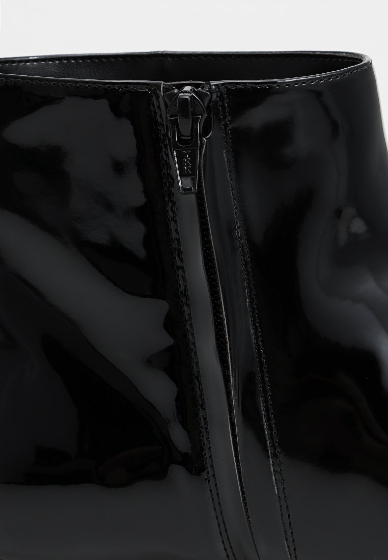 Zbliżenie czarnego lakierowanego buta z widocznym pionowym zamkiem błyskawicznym i szwami wzdłuż krawędzi.