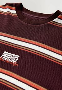 Bordeaux strikket t-shirt med horisontale striber i orange, hvid og brun. Har grafisk tekst "PROVIDENCE" i hvid og orange.
