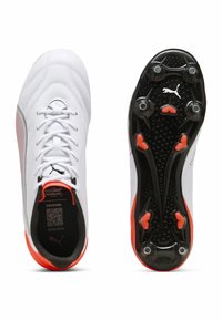 Scarpini da calcio bianchi con accenti rossi, caratterizzati da un design superiore elegante, chiusura con lacci e una suola nera testurizzata con tacchetti arancioni.