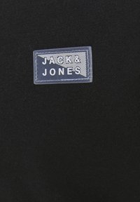 Svart tyg med en transparent rektangulär remsa som har diagonala linjer och vit text i versaler "JACK & JONES".