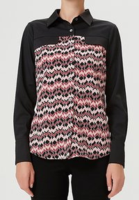 Chemise à boutons avec des manches noires et un devant à motifs en formes géométriques roses, rouges et noires. Col classique et coupe structurée.