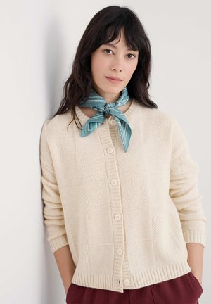 Hellbeige gestrickte Strickjacke mit strukturiertem Muster, ausgestattet mit einer durchgehenden Knopfleiste und gerippten Bündchen. Begleitet von einem türkis gemusterten Schal.