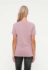 T-shirt z krótkim rękawem, okrągłym dekoltem w jasnoróżowym kolorze z bawełny. Gładka struktura, prosty design, bez widocznych wzorów czy akcentów.