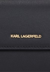 Portafoglio in pelle nera texturizzata con logo dorato "KARL LAGERFELD". Il dettaglio delle cuciture lungo il bordo aggiunge un accento discreto.