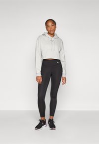 Felpa grigia corta con logo frontale, abbinata a leggings neri a vita alta. Sneakers nere con dettagli rosa completano l'outfit.