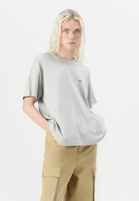 Gray oversized T-shirt in soft fabric, featuring short sleeves, a round neck, and a small pink logo on the chest. Paired with beige cargo pants.