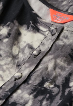 Koszulka w czarno-szarym tye-dye z okrągłym kołnierzykiem, guzikami z przodu i metką z czerwonymi akcentami. Gładka tekstura, casualowy design.