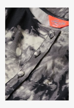 Koszulka w czarno-szarym tye-dye z okrągłym kołnierzykiem, guzikami z przodu i metką z czerwonymi akcentami. Gładka tekstura, casualowy design.