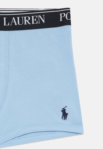 Šviesiai mėlynos medvilninės bokserio trumpikės su juodu juosmeniu, ant kurio yra balti užrašai. Ant kojos yra mažas juodas polo žaidėjo logotipas.