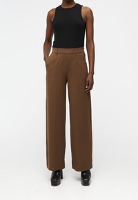 Un débardeur noir à côtes associé à un pantalon marron large et taille haute. Le pantalon possède des poches latérales et est fabriqué dans un tissu lisse.