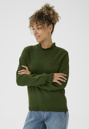 Green knitted sweater with a high neckline, textured zigzag pattern on the chest, and ribbed cuffs. Paired with blue denim jeans.