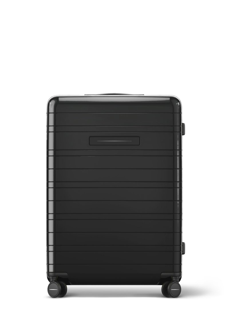 Valise rigide noire avec des rainures horizontales, texture lisse, poignée supérieure et quatre roues pour la mobilité. Le devant présente une poche à glissière.