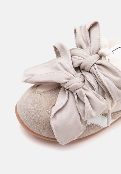 Chaussure en daim beige doux avec de larges lacets en tissu noués et une semelle marron clair sur fond blanc.