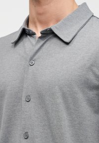 Γκρι μπλουζάκι πόλο με κλασικό γιακά, τρία κουμπιά στη λαιμόκοψη και απαλό, υφασμάτινο ύφασμα, που αναδεικνύει έναν casual αλλά ταυτόχρονα δομημένο σχεδιασμό.