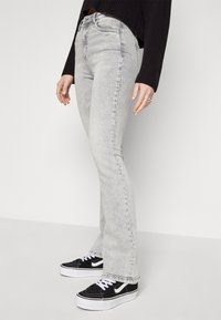Utslåtte lys grå jeans med en falmet tekstur, høy liv, og fem-lommes design, paret med svart og hvite sneakers.