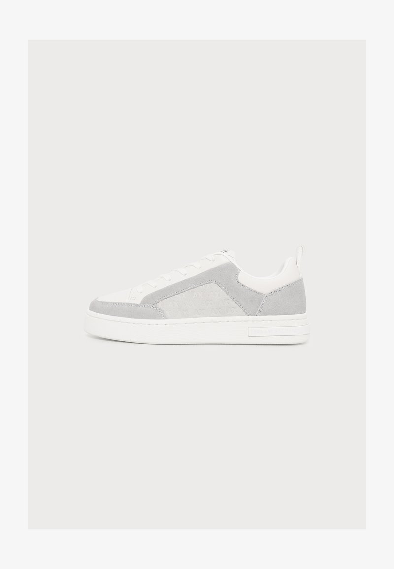 Λευκό sneaker με χαμηλή κορυφή, πάνελ από ανοιχτό γκρι σουέτ, λευκά κορδόνια και χοντρή λευκή σόλα σε απλό ανοιχτό φόντο.