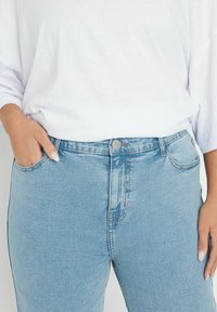 Lichtblauwe denimjeans met een hoge taille, voorzakken en een zilveren knopenclosure. De stof heeft een verouderde textuur en een lichte vervaging.