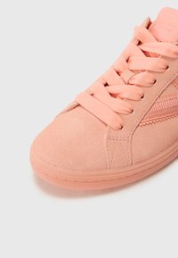 Light pink suede sneaker with smooth texture, flat laces, and a translucent rubber sole. Features a side design element in matching color.