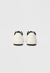 Weiße Sneakers mit schwarzen Akzenten, ausgestattet mit einem glatten Lederobermaterial, abgerundeter Form, gepolstertem Kragen und einer strukturierten schwarzen Sohle.