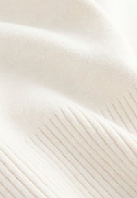 Mäkká, smotanovo sfarbená rebrovaná pletenina s jemnými záhybmi a textúrnymi variáciami.