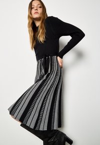 Czarny, prążkowany top z długim rękawem zestawiony z plisowaną spódnicą w pionowe czarno-białe wzory. Czarny, sięgający do kolan zestawionych butów dopełnia całość.