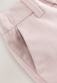 Pantalon en tissu texturé rose clair avec passants de ceinture, poche latérale et détails de couture visibles.