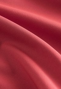 Tissu rouge lisse avec un tissage diagonal subtil et de légers plis créant des ombres douces et des reflets délicats sur la surface.