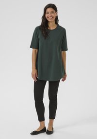 Donkergroen, kortemouwtop met een ronde halslijn en een relaxte pasvorm, gecombineerd met zwarte slim-fit broeken en zwarte ballerina's. Eenvoudig ontwerp.