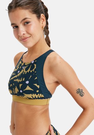 Crop top sportif avec un design multicolore dans des teintes de marine, doré et violet, fabriqué dans un matériau extensible avec une bande solide en bas.