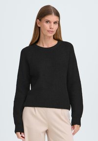 Pull en tricot côtelé noir avec un col rond, des manches longues et une coupe décontractée. Le matériau semble doux, avec une surface texturée.