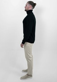 Zwarte coltrui, slim fit ontwerp, beige chino's, lichtgekleurde instappers, textiel met structuur. Zijaanzicht, effen achtergrond.