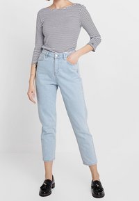 Randig långärmad skjorta i svart och vitt, matchad med ljusblå högmidjade jeans. Svarta loafers med dekorativ accent.