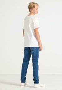 T-shirt bianca in cotone con maniche corte, abbinata a jeans blu in denim e sneakers bianche, vista da dietro. Design semplice, senza fantasie.