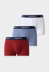 Trois paires de boxers pour hommes Lacoste en blanc, bleu et rouge avec des ceintures bleu marine ornées du logo blanc Lacoste.