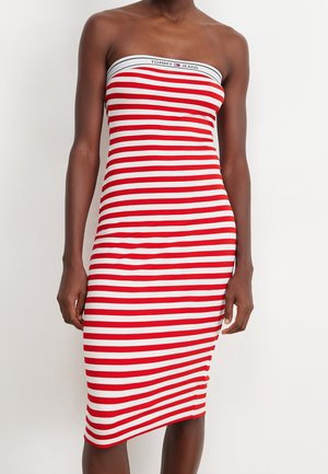 Tummaihoinen henkilö, jolla on yllään olkaimeton, punavalkoraidallinen midi-mekko, jonka yläosassa on "Tommy Jeans" -logo.