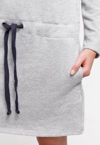 Robe sweat-shirt grise avec une taille à cordon et des poches latérales. Fabriquée dans un matériau doux avec une texture lisse.