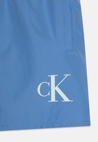 Lys blå shorts i et glat stof med et stort hvidt "cK" logo. Inkluderer sidelommer og et rent, minimalistisk design.