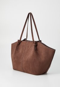Brun ruskinds totebag med en struktureret form, der har lange håndtag og kontrastsyninger langs kanterne. Ingen yderligere udsmykninger.