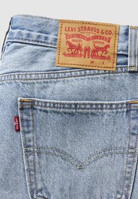 Poche arrière d’un jean en denim bleu clair avec un patch en cuir de la marque Levi Strauss & Co. et une étiquette en tissu rouge Levi's sur le côté de la poche.