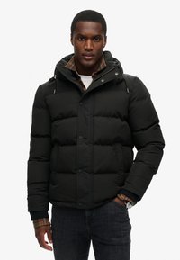 Czarna, puchowa kurtka z kapturem, z zapięciem na guziki i kieszeniami bocznymi. Podszewka zawiera detal w kratę przy mankietach.