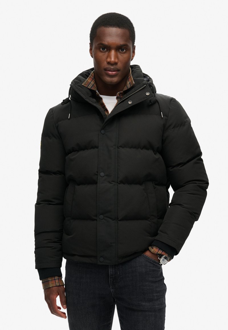 Czarna, puchowa kurtka z kapturem, z zapięciem na guziki i kieszeniami bocznymi. Podszewka zawiera detal w kratę przy mankietach.