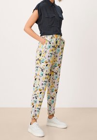 Zwarte short-sleeve shirt met twee zakken, gecombineerd met lichte broek met bloemenpatroon in geel, blauw en zwart. Witte sneakers maken de look compleet.