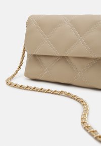 Borsa a spalla trapuntata beige con cuciture crema e una tracolla in oro, caratterizzata da una forma rettangolare e una chiusura a pattina.