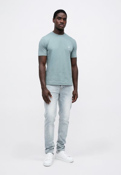 Svijetloplavi kratki rukav majica s okruglim izrezom i malim logotipom. Uparena s svijetlim trapericama i bijelim tenisicama. Jednostavan, ležeran dizajn.