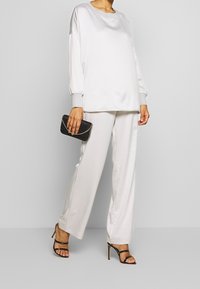 Top largo de satén blanco con detalles en gris, combinado con pantalones de satén blanco y un clutch negro. La modelo lleva tacones negros con tiras.