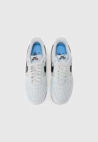 Nike Air Force 1 sneakers with white leather upper, black accents, blue inner lining, perforated toe, and flat white laces.