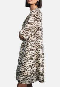 Zebra-Print-Kleid in Beige und Braun, knielang, mit kurzen Ärmeln und lockerer Passform. Glatte Textur mit fließendem Design.
