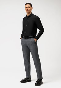 Chemise noire à manches longues, assortie à un pantalon gris à motifs et des chaussures noires. Tissu texturé ; design ajusté.