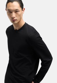 Czarna koszula z długim rękawem wykonana z gładkiej tkaniny, z okrągłym dekoltem. Posiada subtelne detale szycia oraz dopasowany krój.