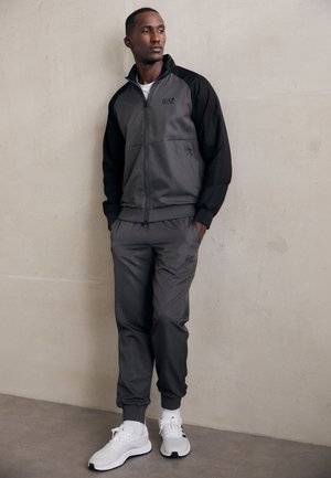 Gray athletic tracksuit with black accents; zip-up jacket and elastic cuff pants; soft fabric; branded logo on chest; paired with white sneakers.